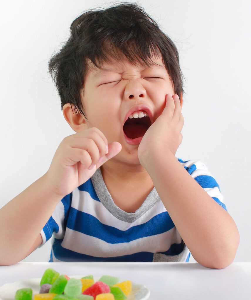 Enfant tenant sa mâchoire en signe de douleur face à un plat de bonbons sur le site de la clinique dentaire Deslauriers Pissardo Jacques.
