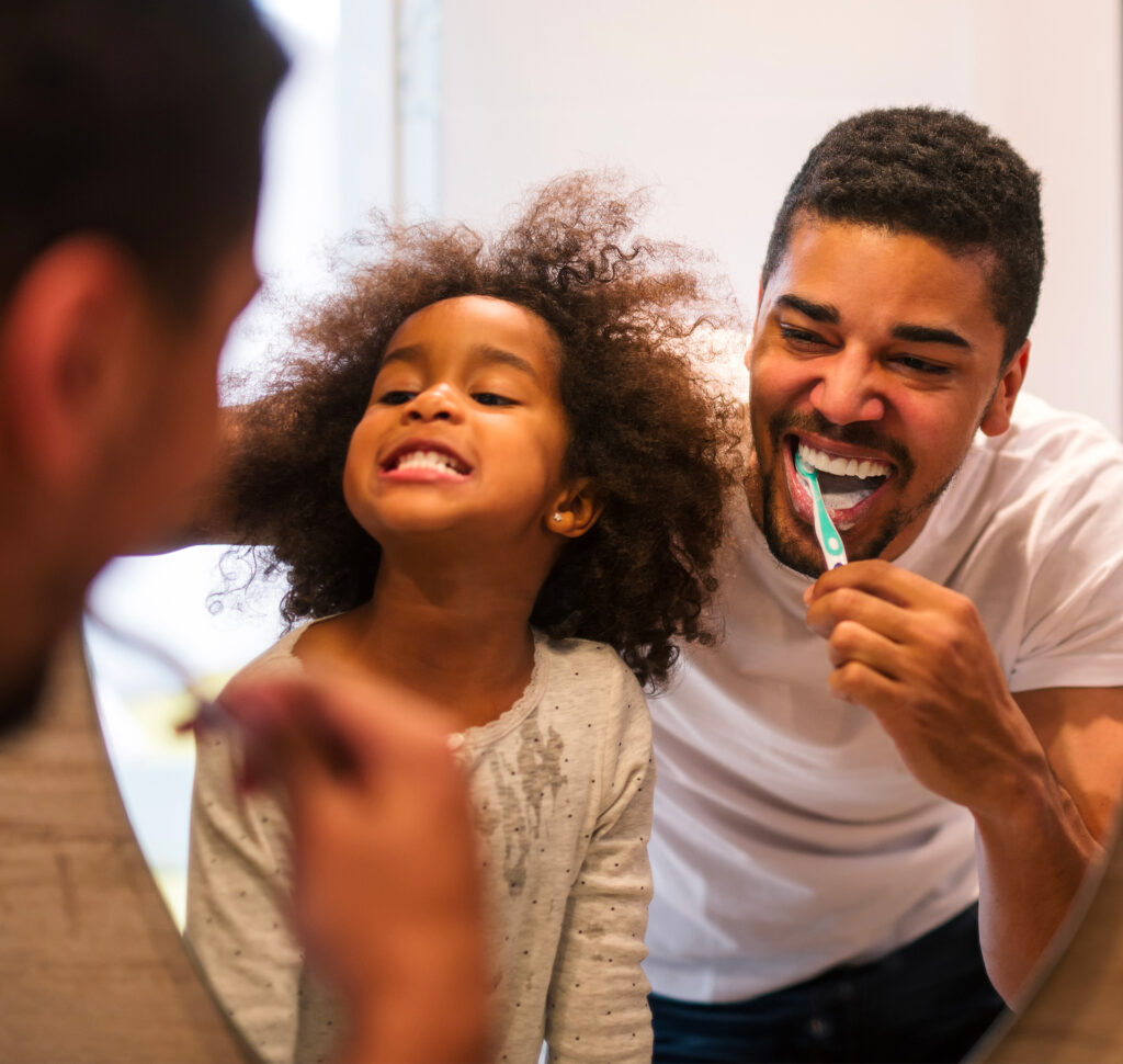petite fille aux cheveux bouclés avec son papa, se brossant les dents après la première visite chez le dentiste